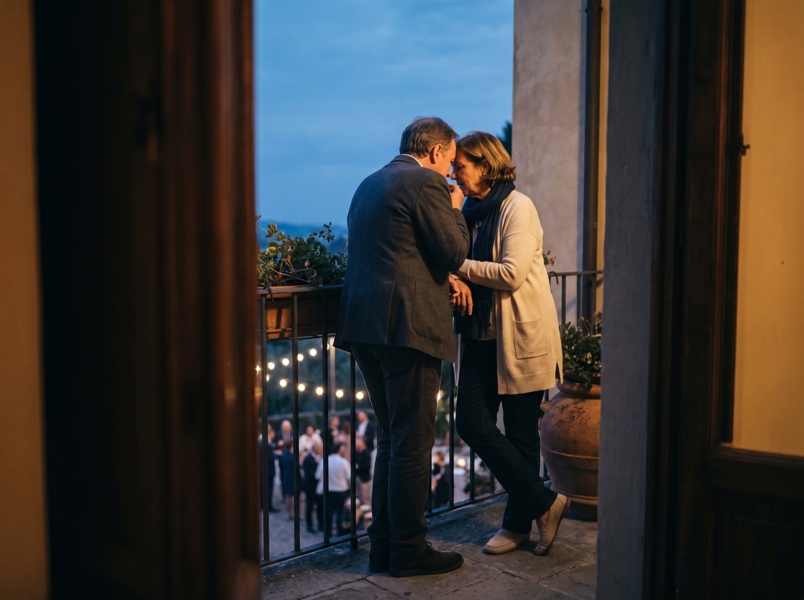 Two guests talking on a balcony at the edge of a gathering